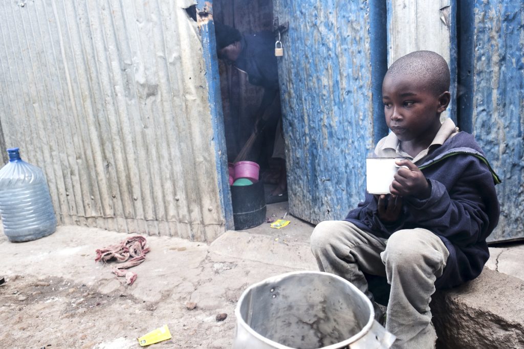 Benjamin, 9, is drinking freshly cooked tea in front of his home while his mother is cleaning the room.