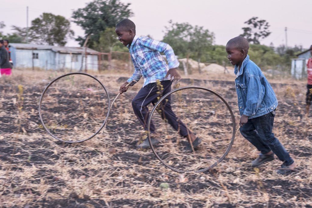 Daniel 12 and Benjamin 9 play with the wheel rims in the field behind their home in rural Kenya.